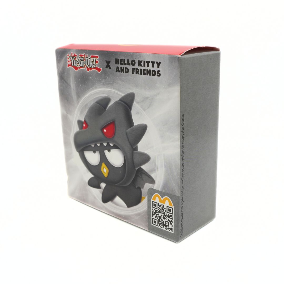 A boxed collectible figure from the McDonald's Happy Meal, featuring a collaboration with Yu-Gi-Oh! and Hello Kitty and Friends. The packaging is gray with a clear window showing a black cartoon monster with red eyes and a yellow mouth, alongside the McDonald's logo and a QR code.