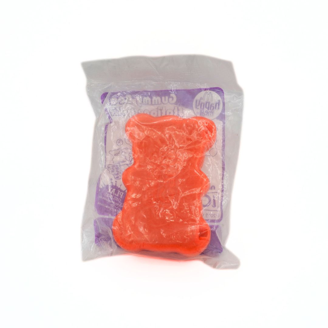 Orange gummy bear in a clear plastic packaging with a purple label on a white background